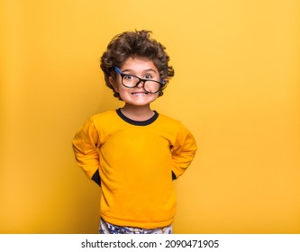 Funny surprised little child boy in glasses looking in camera isolated on yellow background. Kindergarden kid smiling. Education for smart children.