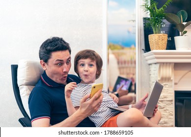 Funny and surprised young father with preschooler son sit on chair using laptop relax, holding smartphone, have fun together. Dad and little boy child enjoy weekend at home, busy with gadgets. - Shutterstock ID 1788659105