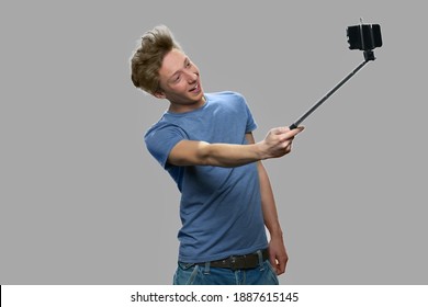 Funny Teen Boy Using Selfie Stick. Stylish Teen Guy Taking Selfi With Monopod Against Gray Background. Youth And Modern Technology Concept.