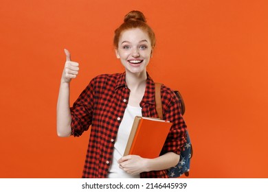 Funny Teen Redhead Student Girl 17s In Casual Red Checkered Shirt Backpack Posing Isolated On Orange Wall Background. Education In High School University College Concept. Hold Books, Showing Thumb Up