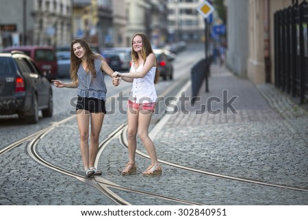 Funny teenage girls together walking on the pavement on the street.