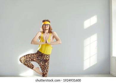 Funny Thin Long Haired Male In Yellow Undershirt And Leopard Pattened Pants Standing In Meditation Position Practicing Yoga Over Light Grey Wall Background, Copy Spa. Funny Active Sport Lifestyle