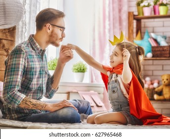 Funny Time! Father And His Child Are Playing At Home. Cute Girl Holding Paper Crown On Stick And Pretend Of Princess. Dad Kisses Hand Of His Daughter. Family Holiday And Togetherness.