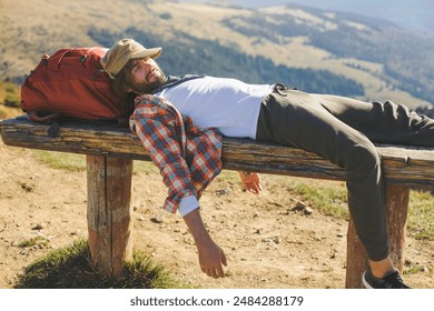 A funny and tired hiker in a plaid shirt and hat lying on a wooden bench with a backpack, set against a scenic mountain landscape. Perfect for themes of adventure, humor, exhaustion, and outdoor - Powered by Shutterstock