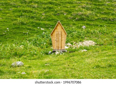 Funny toilet in the form of a house with a roof in the middle of a green field