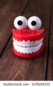 Funny Toy Chattering Teeth Toy With Big Eyes On A Wooden Background With Copy Space. Plastic Red Mouth With White Fangs Is A Concept Of Oral Hygiene And Healthy Teeth