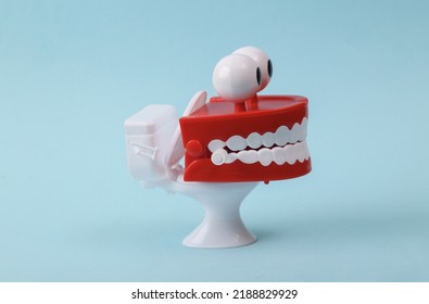 Funny Toy Clockwork Jumping Teeth With Eyes On Toilet, Blue Background.