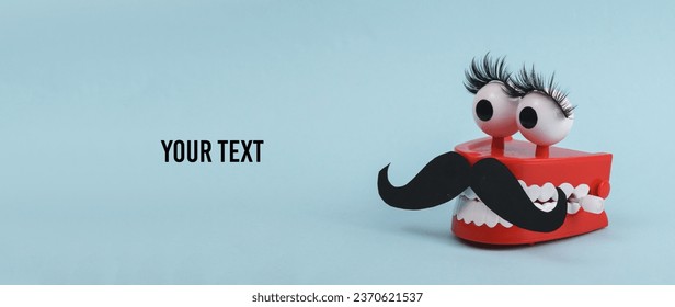 Funny toy clockwork jumping teeth with eyes and false eyelashes, mustache on blue background. Transgender, indeterminate gender concept. Copy space