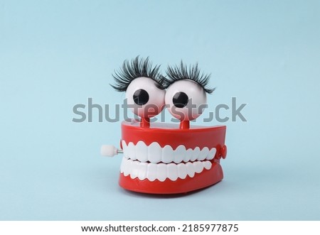 Funny toy clockwork jumping teeth with eyes and false eyelashes on blue background. Beaty concept