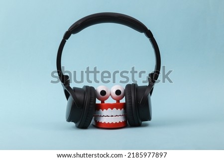 Funny toy clockwork jumping teeth with eyes listen music in stereo headphones on blue background.