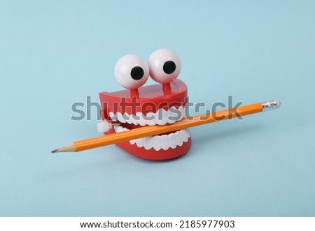 Funny toy clockwork jumping teeth with eyes holding pencil on blue background.