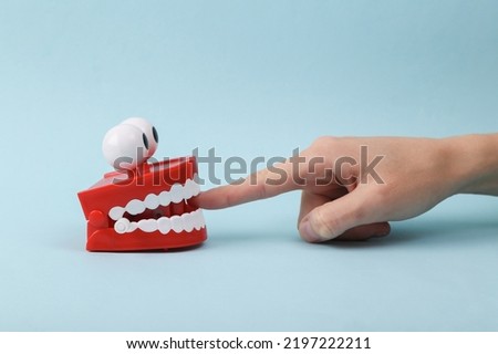 Funny toy clockwork jumping teeth with eyes biting finger of hand, blue background.
