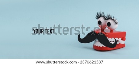 Funny toy clockwork jumping teeth with eyes and false eyelashes, mustache on blue background. Transgender, indeterminate gender concept. Copy space