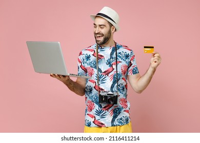 Funny Traveler Tourist Man In Summer Clothes Hat Using Laptop Pc Computer Booking Hotel Hold Credit Bank Card Isolated On Pink Background. Passenger Traveling On Weekends. Air Flight Journey Concept