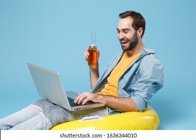 Funny Traveler Tourist Man In Yellow Clothes Isolated On Blue Background. Passenger Traveling Abroad On Weekend. Air Flight Journey Concept. Sitting In Inflatable Ring Work On Laptop Hold Beer Bottle