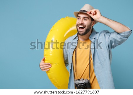 Funny traveler tourist man in yellow clothes with photo camera isolated on blue background. Passenger traveling abroad on weekends. Air flight journey concept. Hold inflatable ring, looking aside