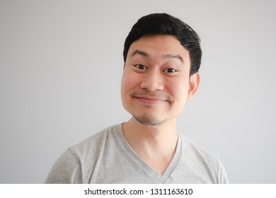 Funny tricky awkward smirk face of Asian man in grey t-shirt.