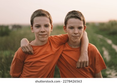 Funny twin brother boys in orange t-shirt playing outdoors on field at sunset. Happy children, lifestyle.