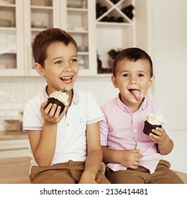 Funny Two Brother Male Kids Are Sitting Together At The Kitchen Table And Eating Cupcakes.