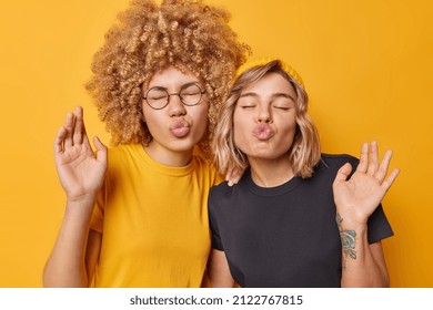 Funny two female friends have fun pout lips keeps eyes closed dressed in casual t shirts foolish around make grimace isolated over bright yellow background. Friendship and free time concept.