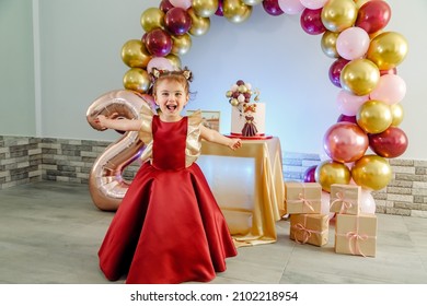 Funny Two Year Old Baby Girl With Red Clothes Having Fun In Front Of Her Birthday Cake. Lovely Baby Girl Birthday Photoshoot