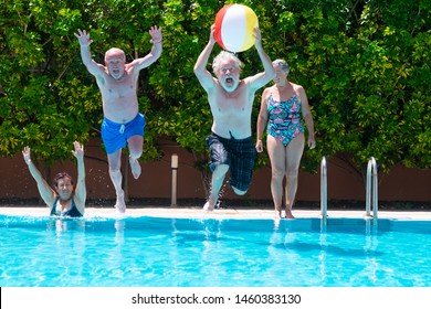 funny view of couples of senior people playing in the blue and transparent water of the swimming pool. Man jumps into the pool with a large inflatable ball