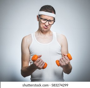 Funny Weak Man Tries To Lift A Weight - Dumbbells His Biceps - Muscle, Isoalted On Gray White.
Nerd Male Exercise- Doing Fitness