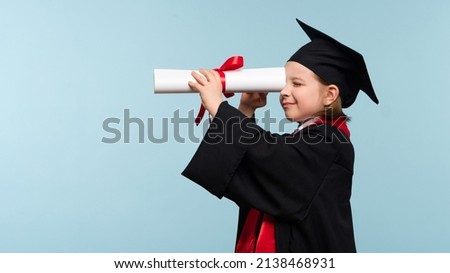 Funny Whizz kid girl wearing graduation cap and ceremony robe on light blue background. Graduate celebrating graduation. Education Concept. Smart child looks to the future through the certificate