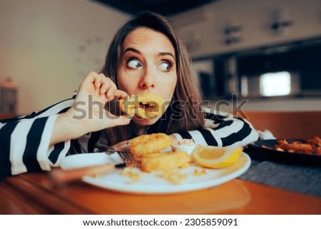 
Funny Woman Holding Calamari Rings in Front of Mouth. Restaurant customer playing with food making silly faces 
