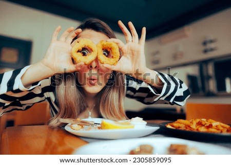 
Funny Woman Holding Calamari Rings in Front of her Eyes. Girl with a sense of humor having an Mediterranean seafood dish
