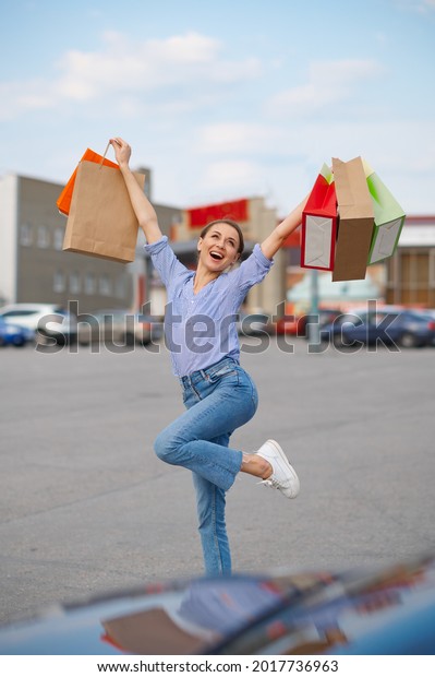Funny woman jumps
with bags on car parking