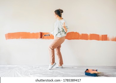 Funny woman painting wall. Rear view of woman with paint roller painting wall. Repair and house renovation concept. - Powered by Shutterstock