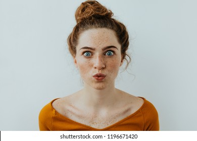 Funny woman portrait. Style. Beautiful blue eyed girl with freckles is pouting lips at camera, on a white background