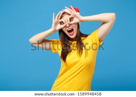 Funny woman Santa girl in Christmas hat posing isolated on blue wall background. New Year 2020 celebration holiday concept. Mock up copy space. Holding hands near eyes imitating glasses or binoculars