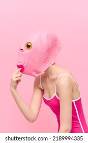 A Funny Woman Wearing A Pink Fish Mask On Her Head Put Her Fingers In Her Mouth With Pink Clothes On A Pink Background. The Concept Of Modern Art Photography