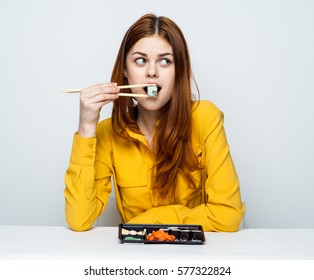 Funny woman in yellow blouse eating sushi at the table. Sushi on sticks, sushi mouth