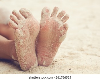 funny woman's feet on the white sand near the sea