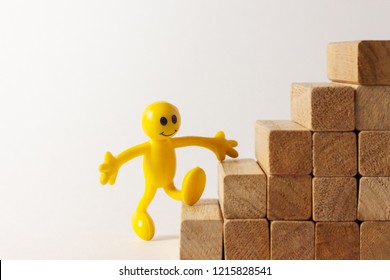 A Funny Yellow Stick Figure Walking Up On Toy Wooden Stairs, Concept To Symbolize Growth, Opportunities, Success, Etc.