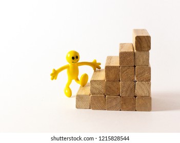 A Funny Yellow Stick Figure Walking Up On Toy Wooden Stairs, Concept To Symbolize Growth, Opportunities, Success, Etc.