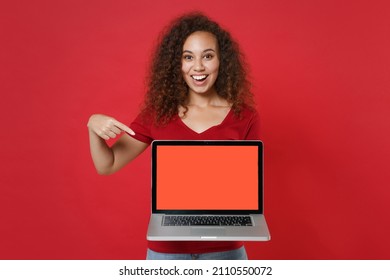 Funny young african american woman girl in casual t-shirt isolated on red background. People lifestyle concept. Mock up copy space. Pointing index finger on laptop pc computer with blank empty screen - Shutterstock ID 2110550072