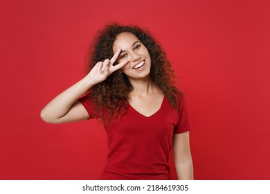 Funny young african american woman 20s in casual t-shirt posing isolated on bright red background studio portrait. People sincere emotions lifestyle concept. Mock up copy space. Showing victory sign