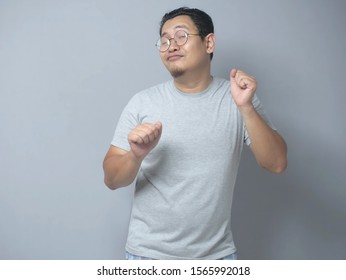 Funny young Asian man dancing happily joyful expressing celebrating good news victory winning success gesture, smiling positive excited emotion while standing against grey wall