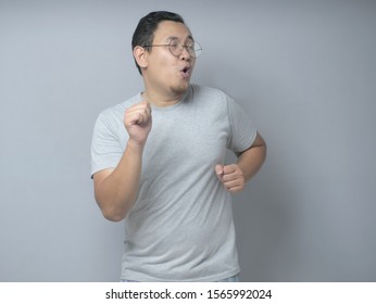 Funny young Asian man dancing happily joyful expressing celebrating good news victory winning success gesture, smiling positive excited emotion while standing against grey wall