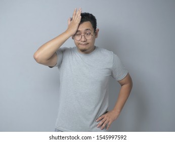 Funny Young Asian Man Shows Regret Gesture, Hits His Forehead, Agains Grey Background