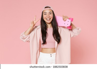 Funny young asian woman 20s in casual clothes, cap posing isolated on pastel pink wall background studio portrait. People lifestyle concept. Mock up copy space. Hold skateboard, showing victory sign - Powered by Shutterstock