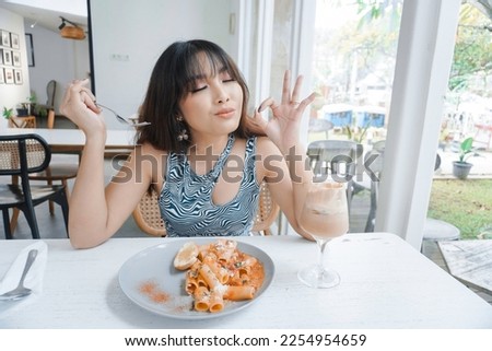 Funny young Asian woman eating tasty pasta in cafe