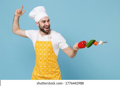 Funny young bearded male chef cook man in apron white t-shirt toque chefs hat isolated on blue background studio portrait. Cooking food concept. Mock up copy space. Hold skewer with fresh vegetables