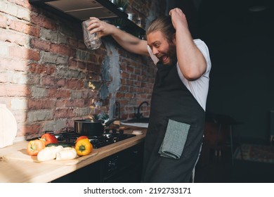 Funny Young Bearded Male Chef In Apron Screaming And Pouring Farfalle Pasta Into Saucepan While Standing At Counter With Fresh Vegetables In Kitchen At Home