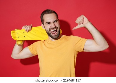 Funny Young Bearded Man Guy In Casual Yellow T-shirt Posing Isolated On Red Wall Background Studio Portrait. People Lifestyle Concept. Mock Up Copy Space. Hold Skateboard Pointing Thumb On Himself