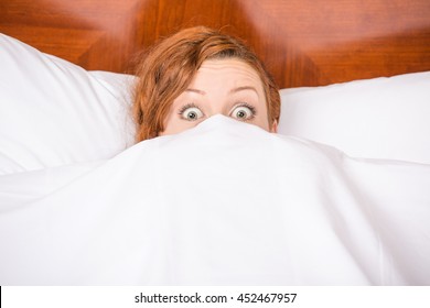 Funny young brunette woman in bed looking and peeking over sheets surprised - Shutterstock ID 452467957